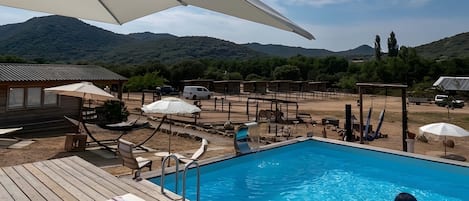 A pool area with lounge chairs, umbrellas, and a view of mountains.
