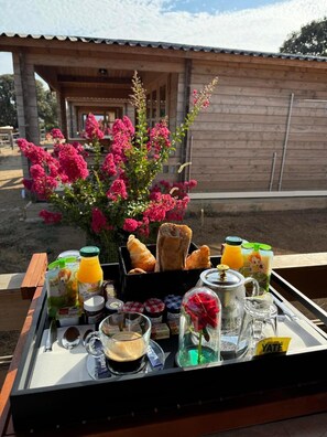 Bandeja de desayuno con cruasanes, jugo, café y un florero sobre una terraza de madera.