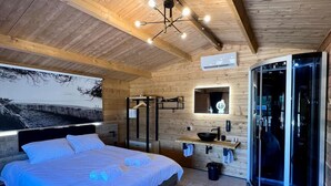 Een moderne slaapkamer met een groot bed, een inbouwkast, een glazen douchecabine en een houten plafond.