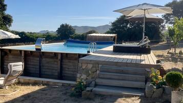 Un patio trasero con piscina, terraza de madera, mobiliario exterior y vista a las montañas.