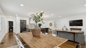 Een moderne keuken met witte kasten, een houten eettafel en een grote plant als middelpunt.