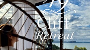 A room with a large window overlooking a scenic view, a hanging chair, and the text "49 Cliff Retreat".
