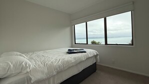 A bedroom with a bed, a large window, and a view of the sea.