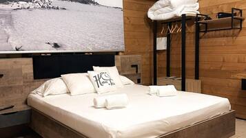 Ein schlafzimmer im Blockhausstil mit einem großen Bett, einer TV-integrierten Kopfteil und Blick auf eine verschneite Landschaft.