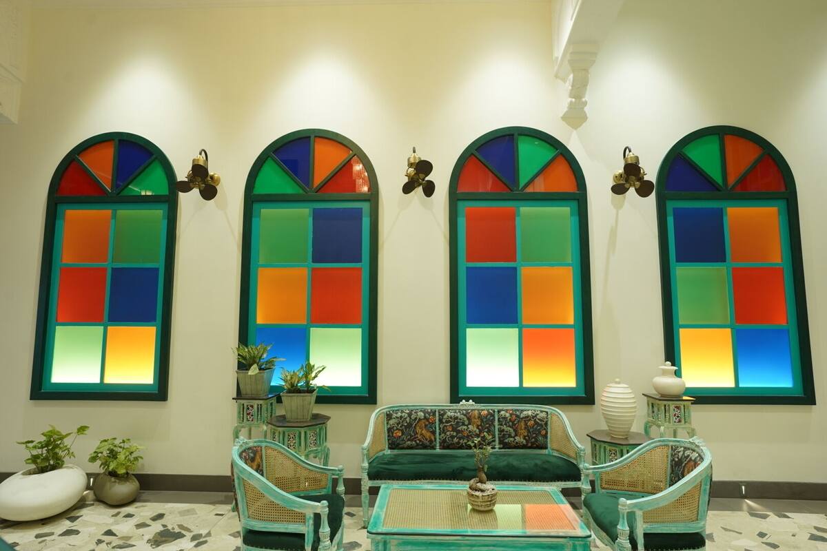 A room with four arched windows with colorful stained glass, a sofa, two chairs, and a small table with a plant.