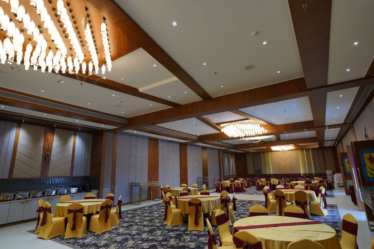 A banquet hall with round tables and chairs, a large chandelier, and a high ceiling with wooden paneling.