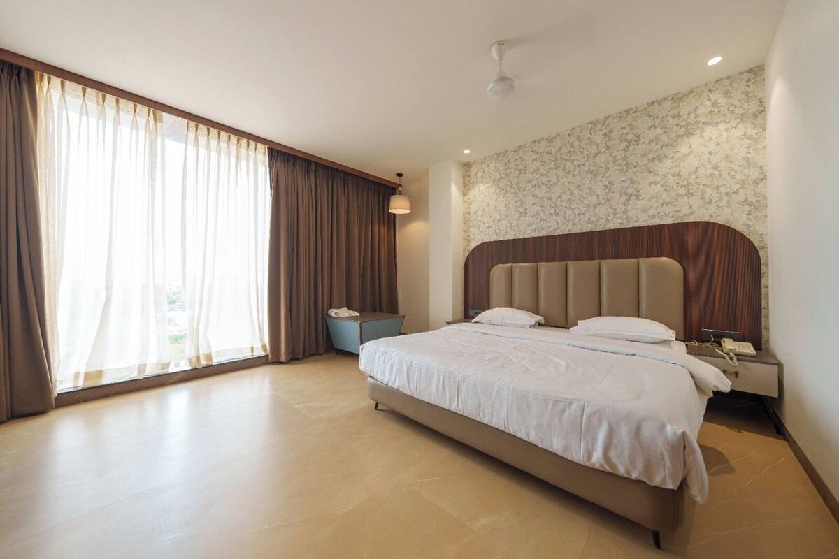 A modern hotel room with a large bed, a bedside table, a nightstand, and a window with curtains.