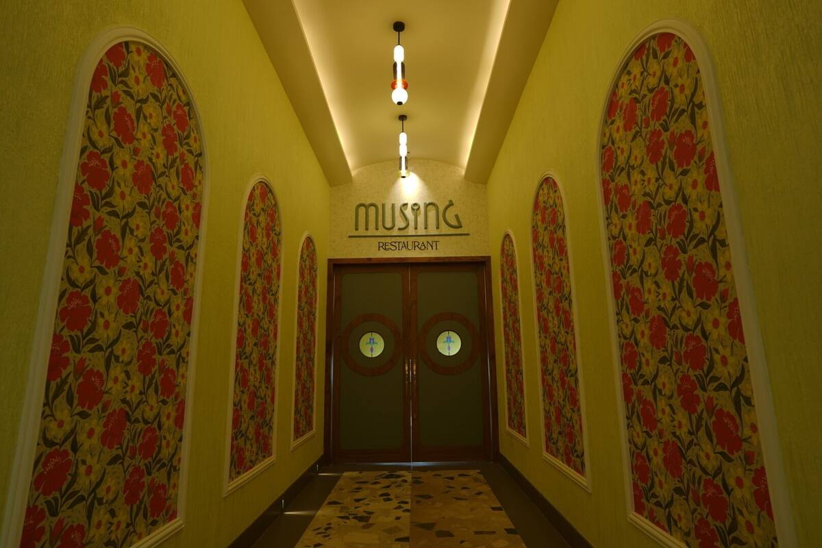 A hallway with floral wallpaper, a sign reading "MUSING RESTAURANT", and a patterned carpet.