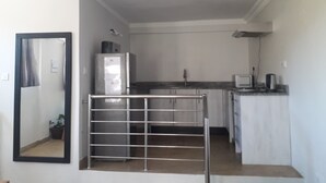 A compact kitchen with a refrigerator, a sink, and a microwave. There is a potted plant and a metal gate in the foreground. - Bedsitter Bed & Breakfast in Nyanga near popular Attractions (Nyanga)
