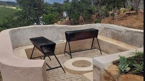A concrete outdoor seating area with two metal grills, a circular fire pit, and a stone planter with plants. - Bedsitter Bed & Breakfast in Nyanga near popular Attractions (Nyanga)