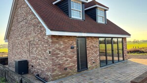 A modern house with a brick exterior, a sloped roof, and a large glass door leading to a covered patio. - Idyllic Studio in Tenterden (Tenterden)