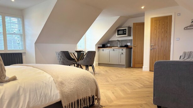 A bedroom with a bed, a grey sofa, a dining table with chairs, a kitchenette, and a door. - Idyllic Studio in Tenterden (Tenterden)