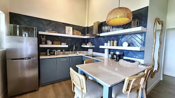 A modern kitchen with a built-in refrigerator, wooden chairs, a dining table, and decorative shelves.