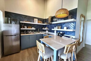 A modern kitchen with a built-in refrigerator, wooden chairs, a dining table, and decorative shelves. - Lantana Sea La Vie - by ZenBreak (Weston)