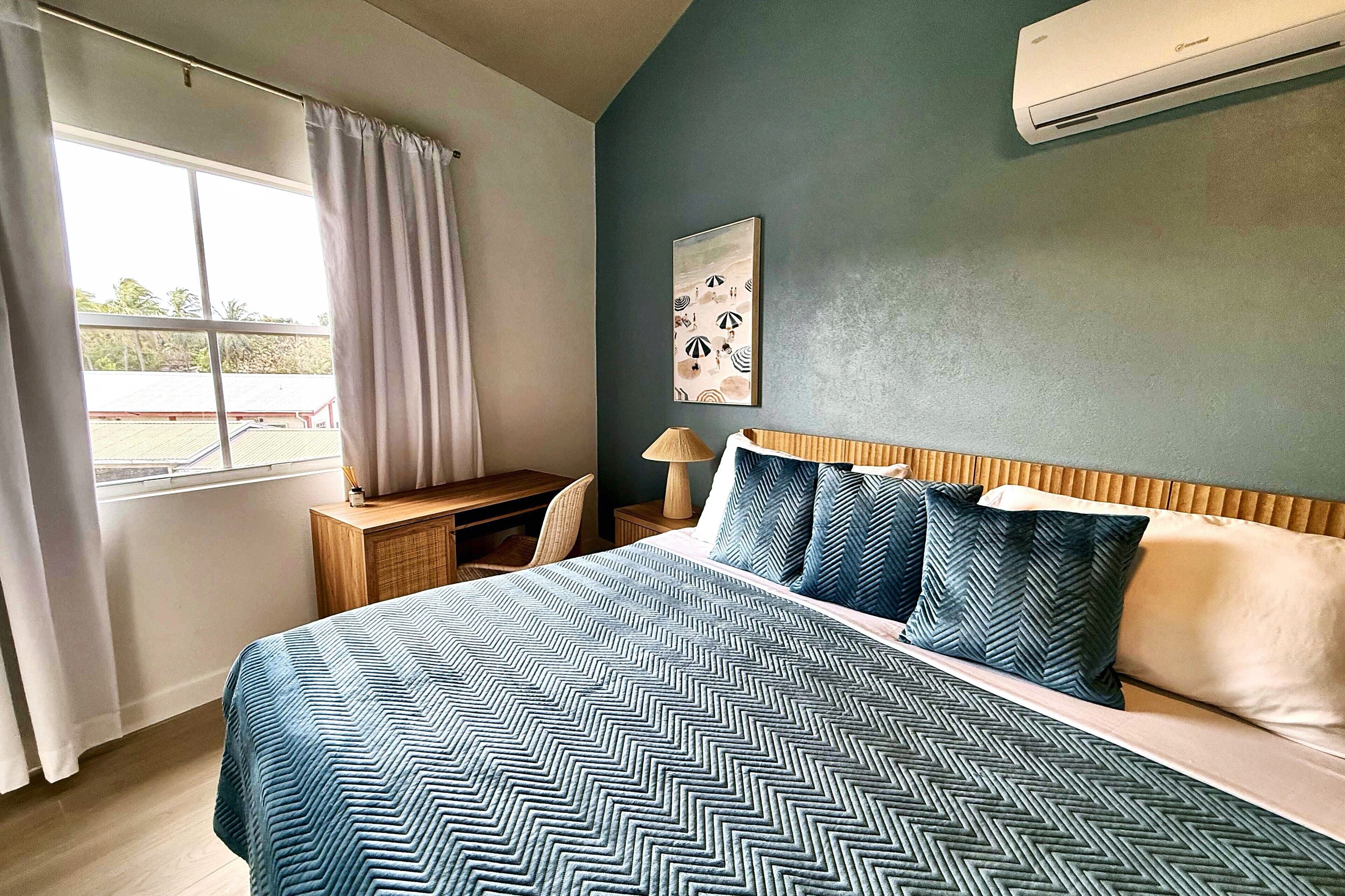 Een slaapkamer met een bed, een bureau, een stoel, een lamp en een raam met gordijnen.