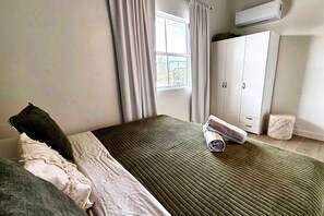 Un dormitorio con cama, armario, ventana con cortinas y aire acondicionado.
