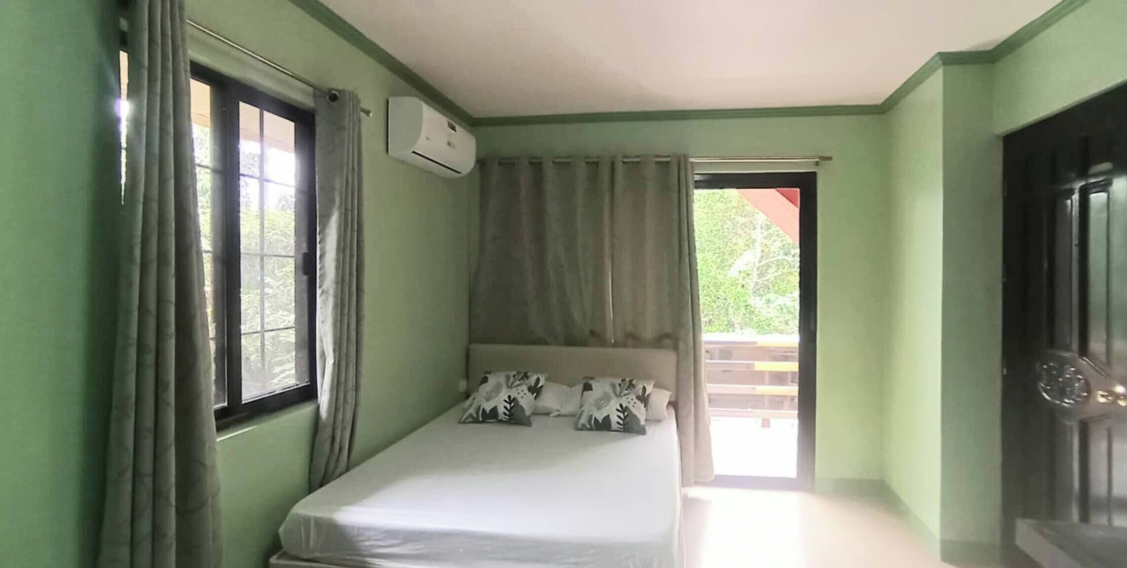 Ein Zimmer mit einem Einzelbett, einem Fenster, einer Klimaanlage und einer Tür zu einem Außenbereich.