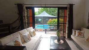 A room with two sofas facing a glass door leading to an outdoor area with a pool and a covered seating area. - Your Tagaytay Escape Here in Mendez, Where Nature, Relaxation, and Fun Await (Mendez)