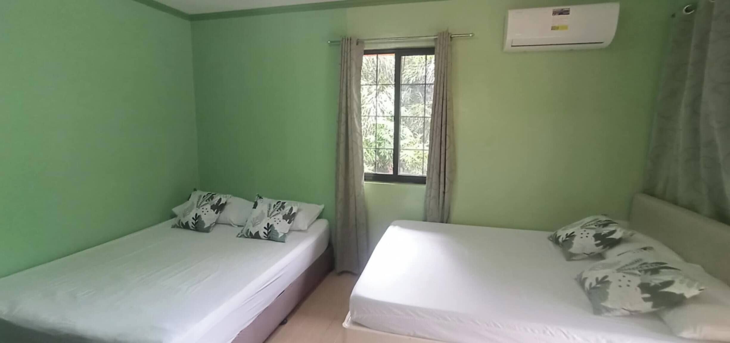 Una habitación con dos camas individuales, una ventana con cortinas y un equipo de aire acondicionado en la pared.