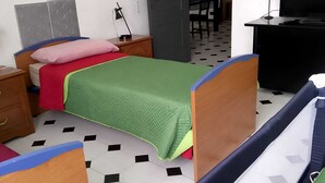 Une chambre avec deux lits simples, un bureau, une chaise, une télévision et une porte donnant sur une autre pièce.