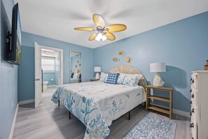 Ein Schlafzimmer mit einem Bett, Nachttischen, einem Deckenventilator, einem Spiegel und einer Kommode.