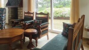 A living room with a stone fireplace, wooden furniture, and a view of a garden through large sliding glass doors.