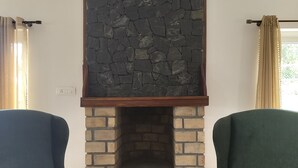 A room with a stone fireplace, two green armchairs, and a wooden floor.