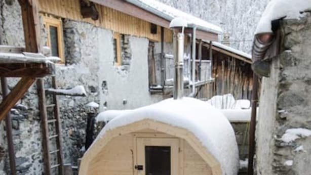 A snow-covered wooden structure with a door and two benches, surrounded by snow and stone walls. - Loft Bonziers - authentic alpine experience (6p, sauna) (Peisey-Nancroix)