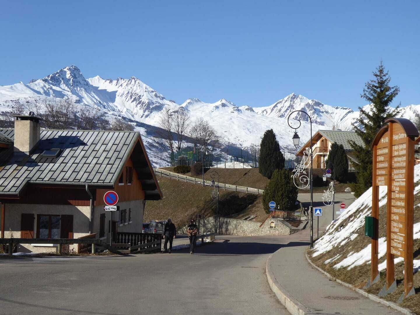 A mountain resort with a wooden building, a signpost with room names, and a view of snow-covered peaks.