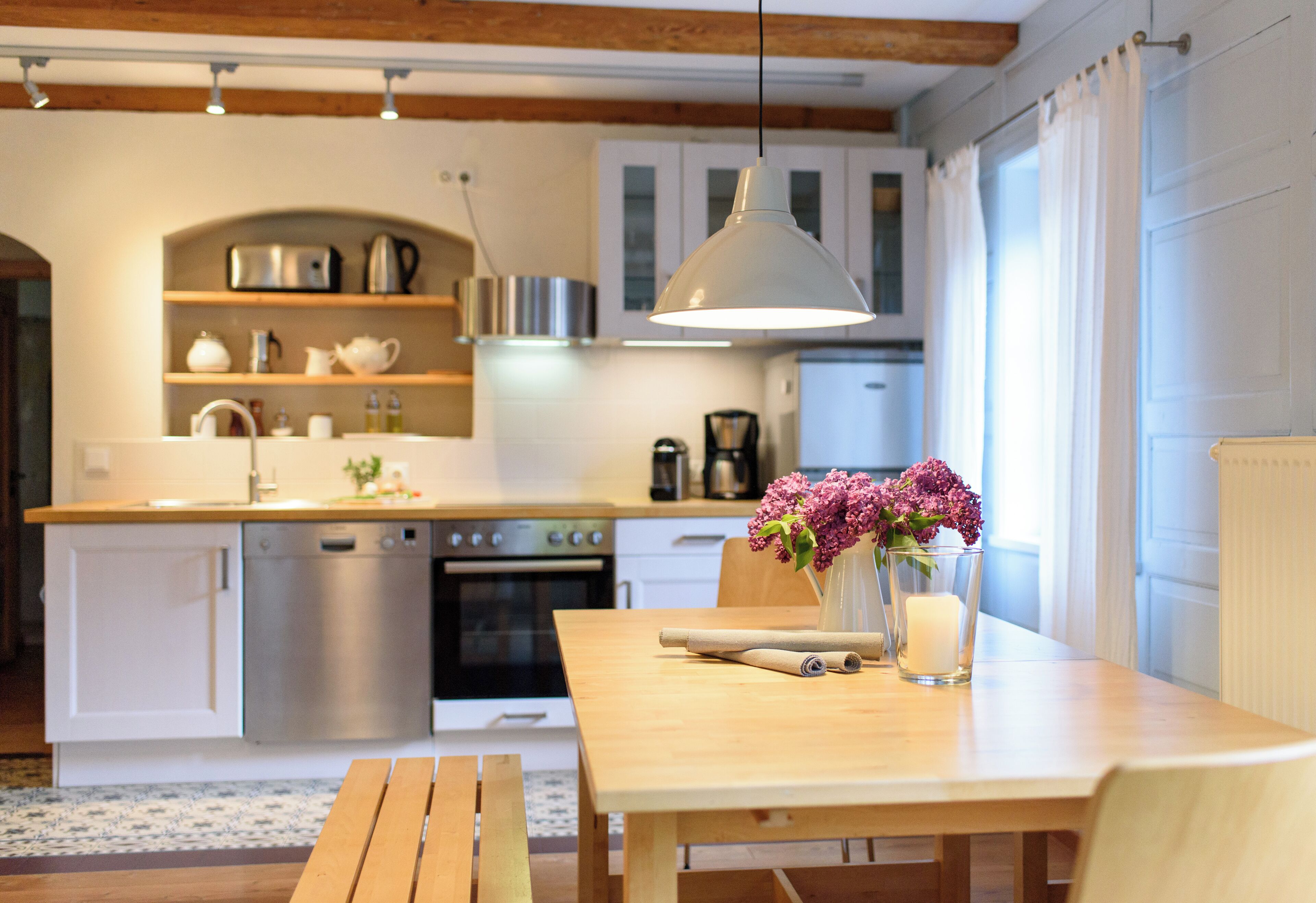 A kitchen with wooden cabinets, a dining table with a vase of flowers, and a hanging light fixture.