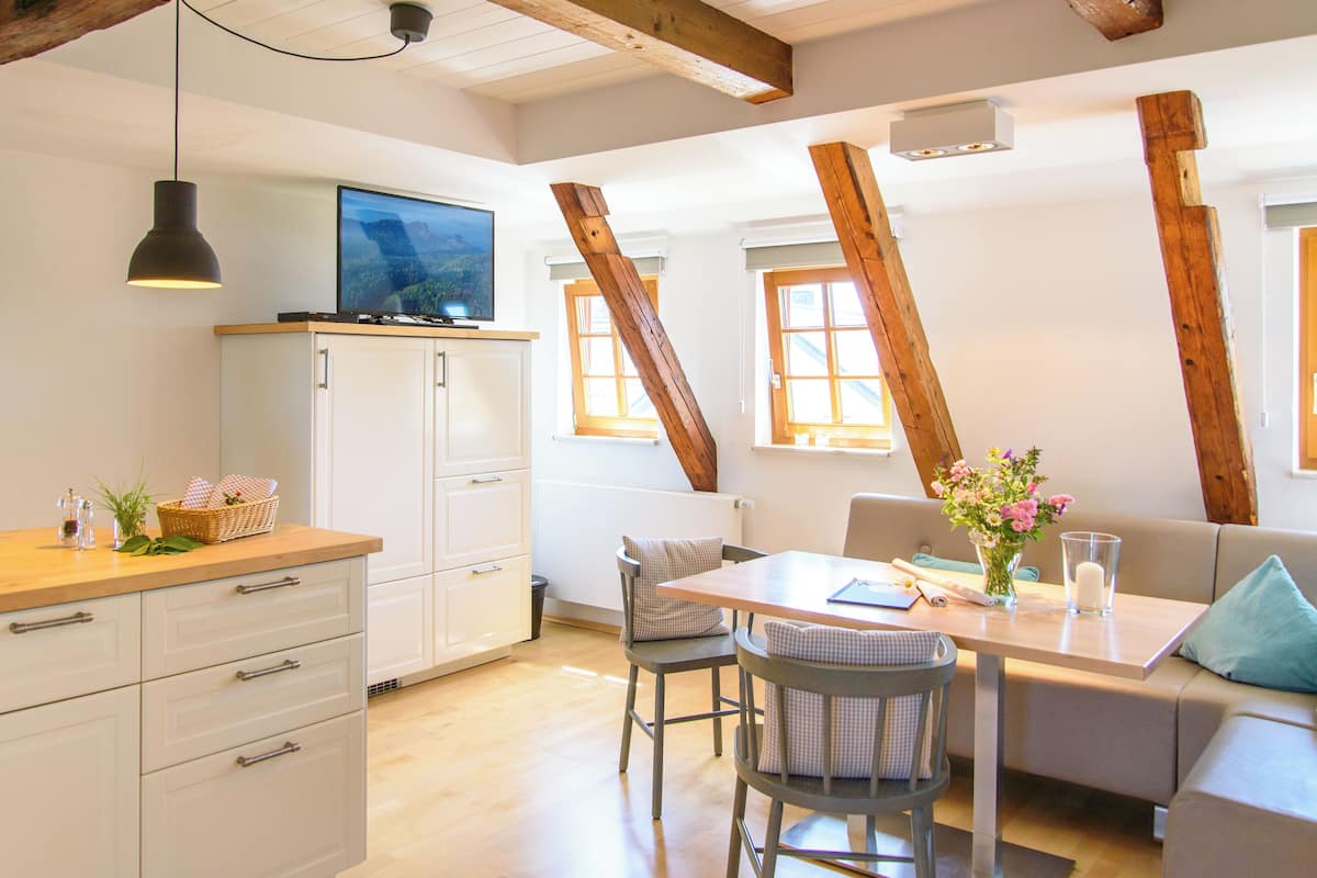 Una cocina moderna con armarios blancos, techo de madera y comedor con mesa y sillas.