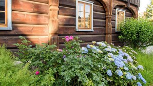 Una cabaña de madera con dos ventanas y un jardín de hortensias y rosas.