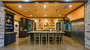 A modern kitchen with a central island, bar stools, a stainless steel refrigerator, and built-in appliances.