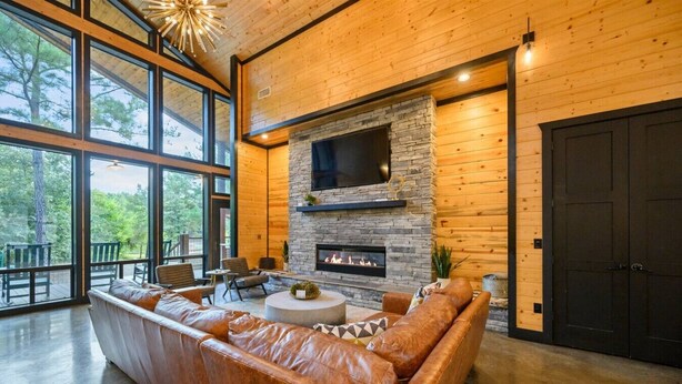 A spacious living room with a stone fireplace, leather sofa, and large windows offering a view of the outdoors.