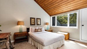 A bedroom with a sloped ceiling, a large window, a bed with a white bedspread, two bedside tables with lamps, and a small wooden chest. - Highlands 24 with Wintergreen Advantage (Wintergreen)