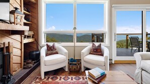 A cozy living room with two white armchairs, a wooden floor, a large window with a view of the mountains, and a fireplace with logs. - Highlands 24 with Wintergreen Advantage (Wintergreen)
