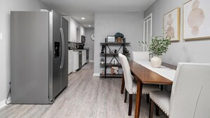 Una cocina moderna con refrigerador empotrado, piso de madera y un comedor con mesa y sillas de madera.