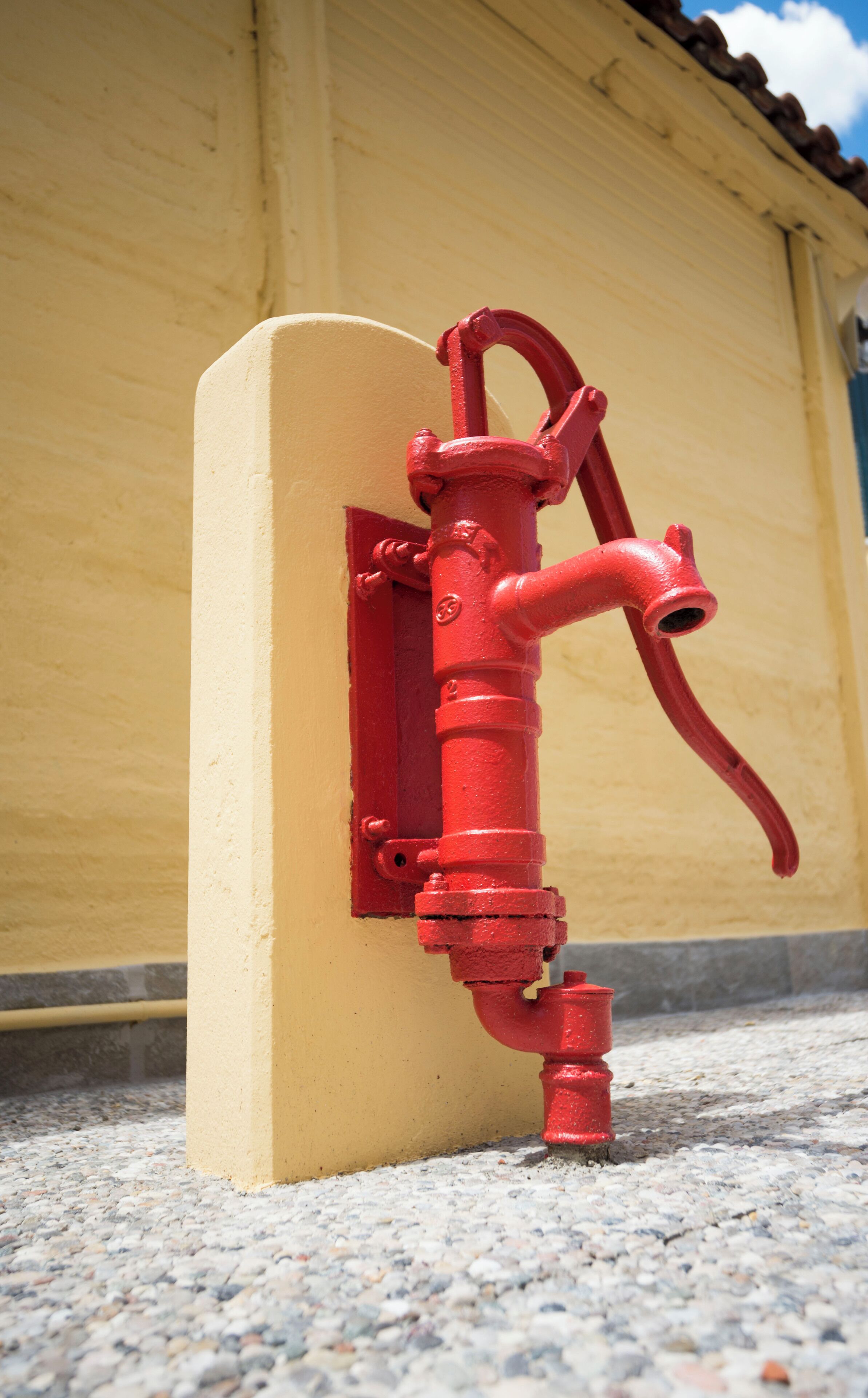 A red fire hydrant mounted on a yellow wall.