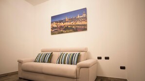 A living room with a beige sofa, two striped pillows, a cityscape painting on the wall, and a brown rug.