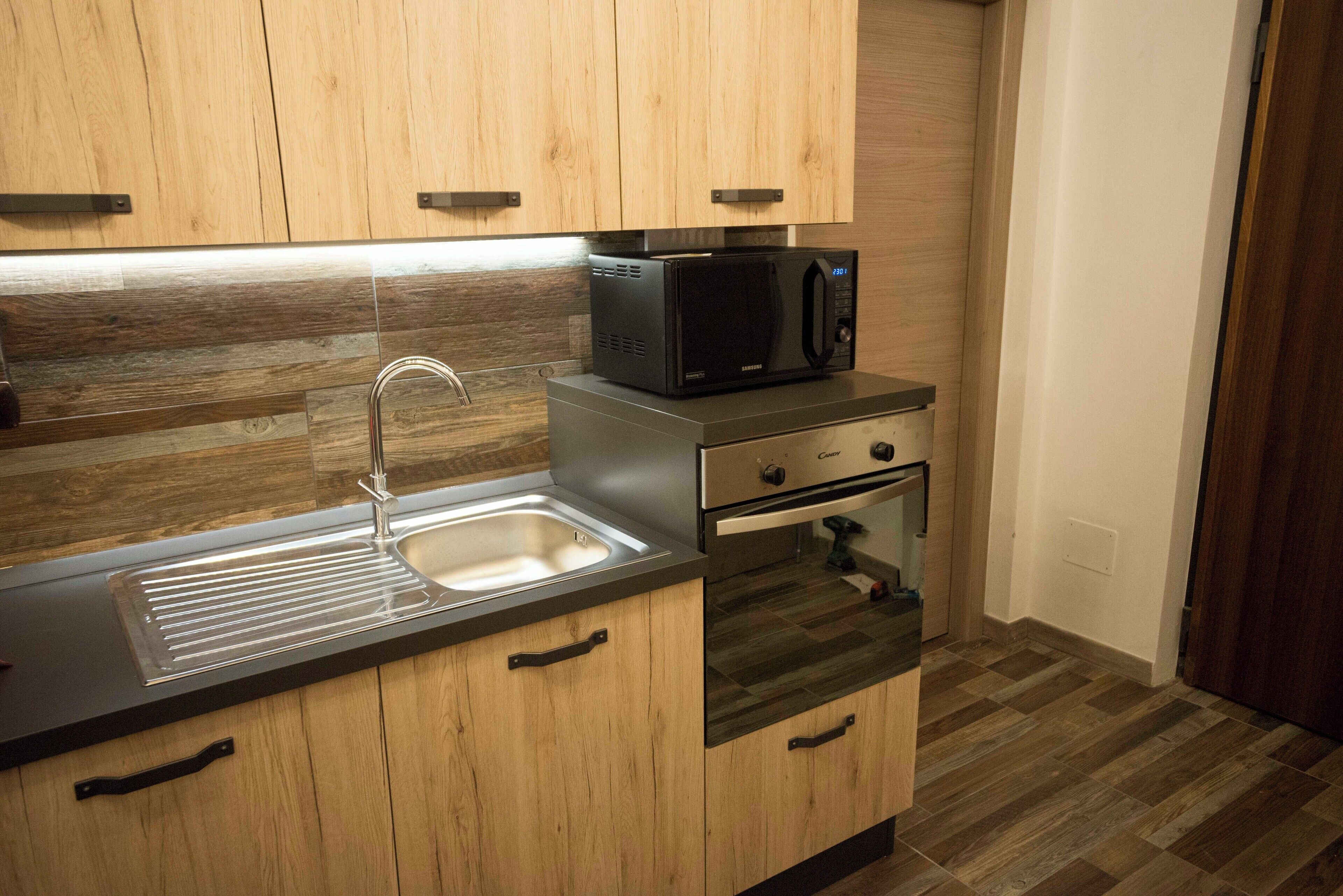 A compact kitchen with wooden cabinets, a stainless steel sink, a microwave, and a built-in oven.