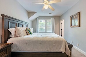 A bedroom with a large bed, a ceiling fan, and a window with blinds.