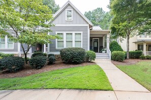 A two-story house with a front porch, a well-maintained lawn, and mature trees.