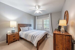 A bedroom with a bed, a nightstand, a dresser, a ceiling fan, and a window with curtains. - 4BR Lake Oconee Gem - Golf Views & Kid-Friendly (Greensboro)