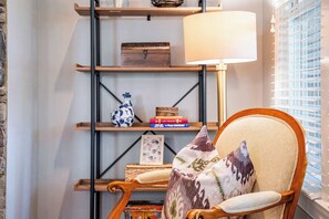 Une pièce chaleureuse avec une chaise en bois, une lampe et une bibliothèque agrémentée d’objets décoratifs.