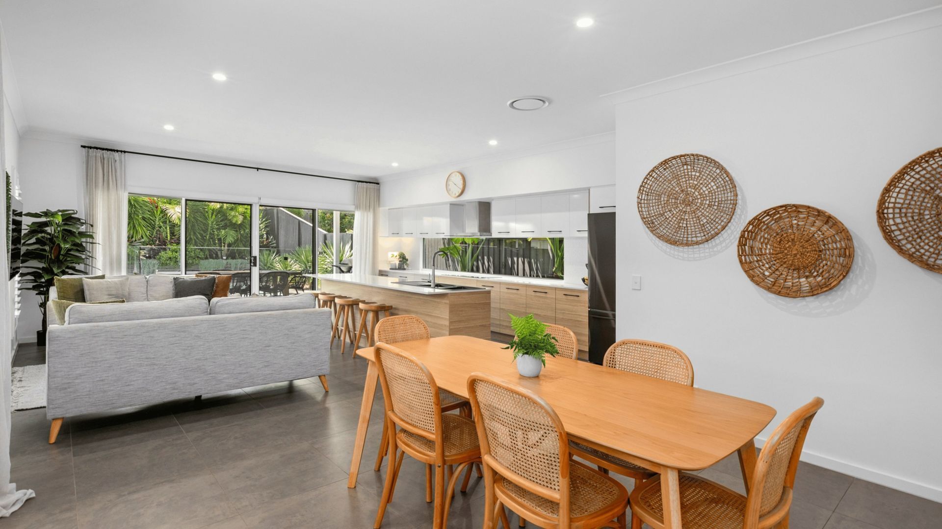 A modern kitchen with white cabinets, a wooden dining table, and wicker wall decor.