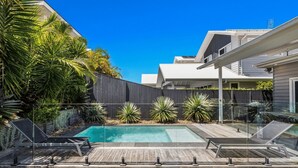 A modern backyard with a swimming pool, wooden deck, and a black fence. - The Palms on Nautilus (Kingscliff)