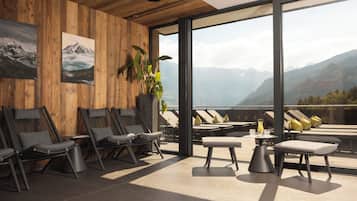 Ein stilvoller Lounge-Bereich mit Holzvertäfelung, Liegesesseln, einer Topfpflanze und Bergblick durch große Fenster.
