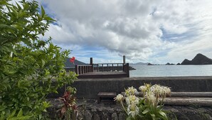 Um cais de madeira que se estende sobre a água, com um muro de pedra e vegetação ao primeiro plano.