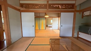 Um quarto japonês tradicional com tatames, portas deslizantes e uma cama ao fundo.