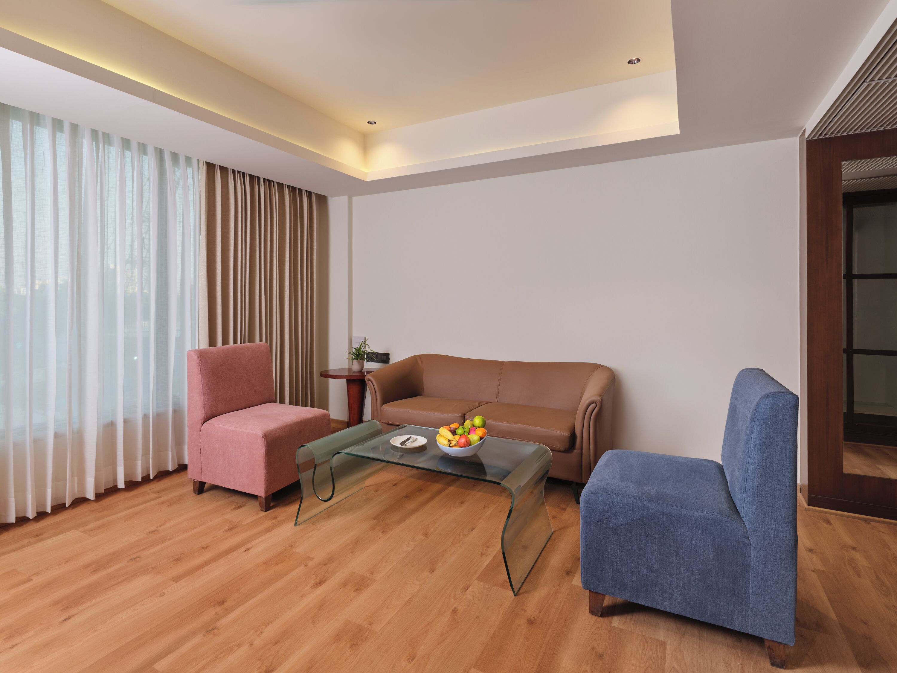 Ein modernes Wohnzimmer mit einem braunen Ledersofa, einem blauen Sessel und einem Glastisch mit Obst.